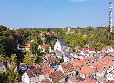 Blick über ein idyllisches Dörfchen mit mittelalterlichem Kern, roten Dächern und Burg