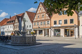 Marktplatz (Ebermannstadt, Fränkische Schweiz) Stadtplatz mit Fachwerkhäusern, einem Brunnen und Geschäften bei sonnigem Wetter.
