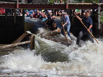 Gruppe von Menschen auf einem Floß in einem Fluss, umgeben von spritzendem Wasser.