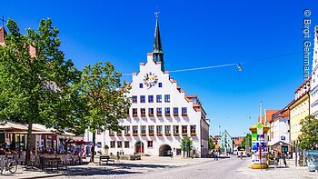 Rathaus (Neumarkt i.d.OPf.) Ein historisches Gebäude mit Giebel und Turm steht auf einem Platz, umgeben von Bäumen und Cafés.