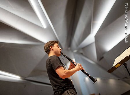 Meisterkurs für Klarinette Schüler Ein junger Mann steht in einem Konzertsaal und spielt Klarinette.
