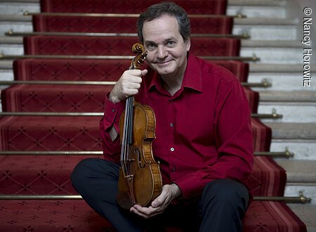 Prof. Christian Altenburger Ein Mann sitzt auf einer Treppe und hält eine Geige vor sich.