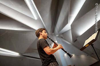 Ein junger Mann steht in einem Konzertsaal und spielt Klarinette.